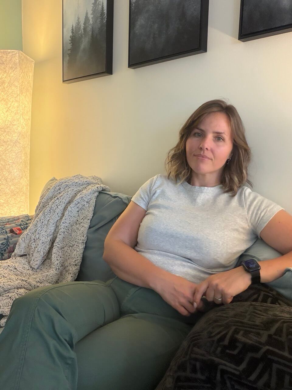 Kate Pozo sitting in a green armchair in a warm living room, with a floor lamp and framed art on the wall