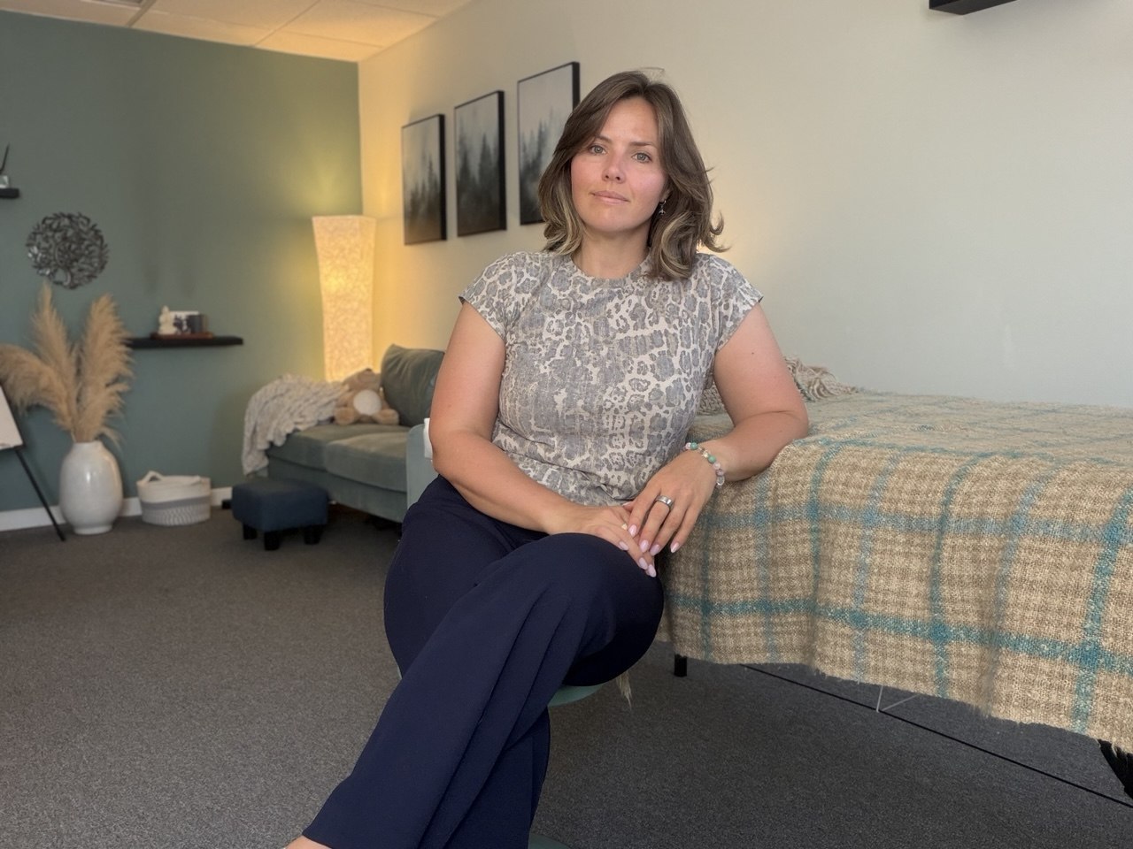 Kate Pozo seated in a calm therapy room with a sofa, floor lamp, framed art, and a cushioned bench with a plaid throw
